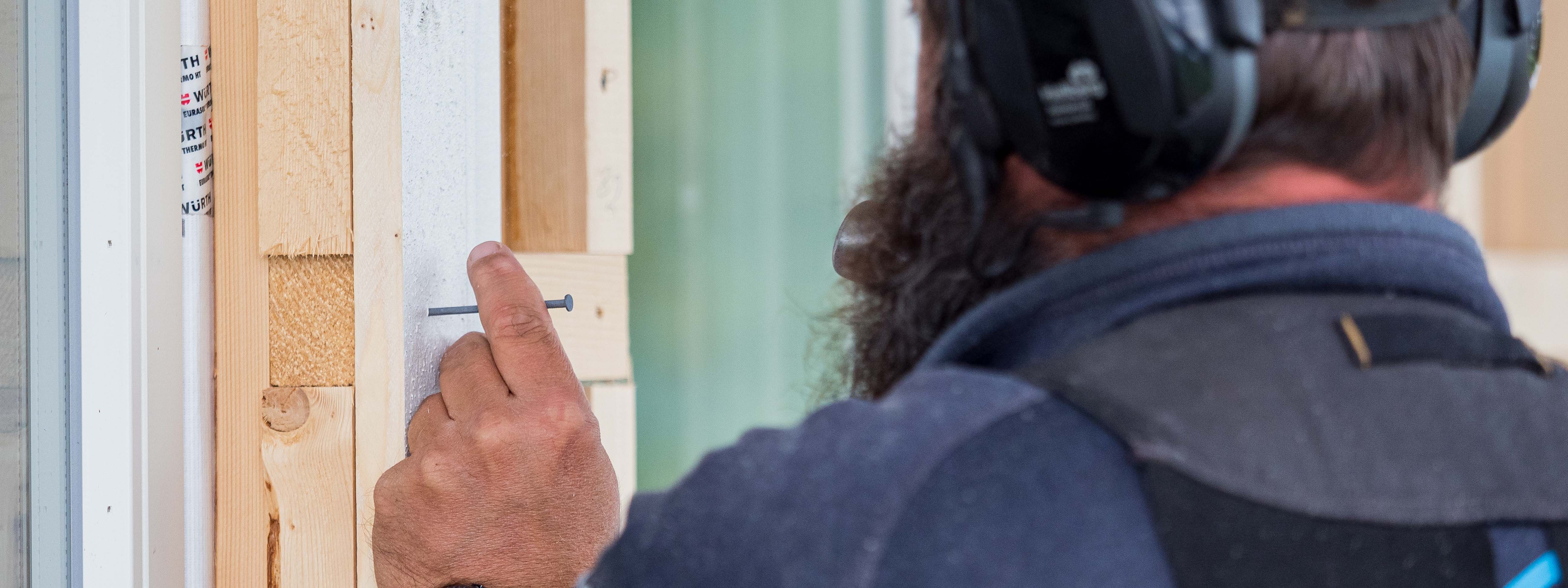 Snekker som hamrer inn kledningsbord på vegg med 1 spiker.