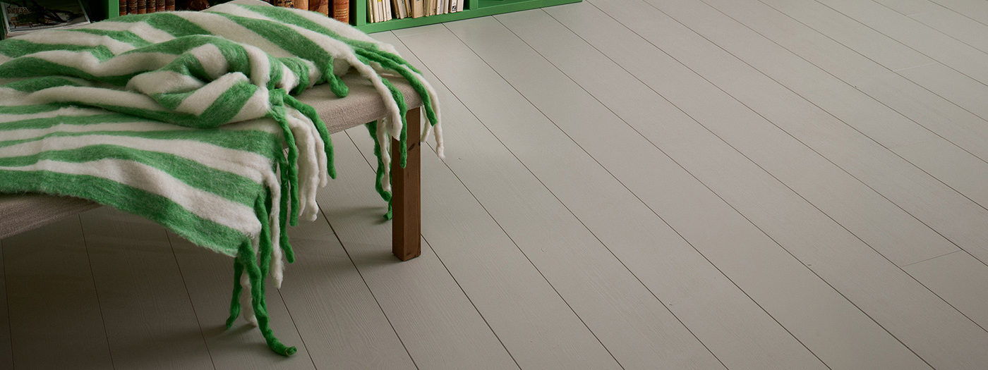 Gråmålat Leva trägolv och en bänk med vit- och grönrandig filt