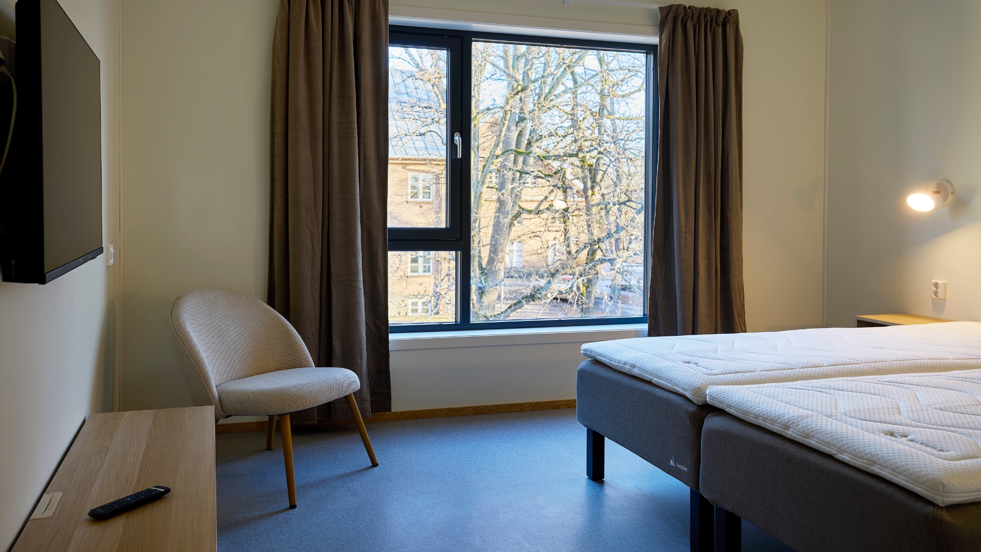 Hotelzimmer mit Doppelbett, TV-Bank und Blick zum Fenster.