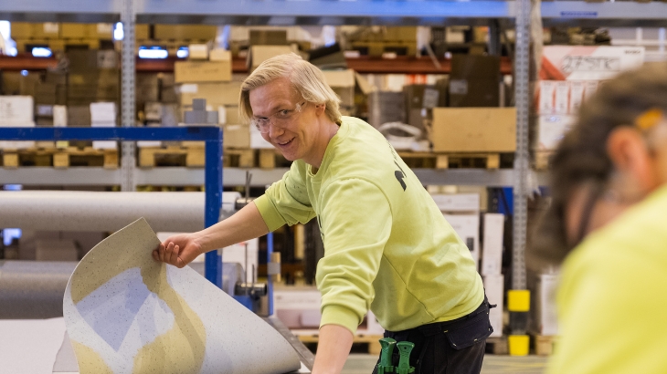 Fabrikarbeiter, der einen ausgerollten Bodenbelag hält.