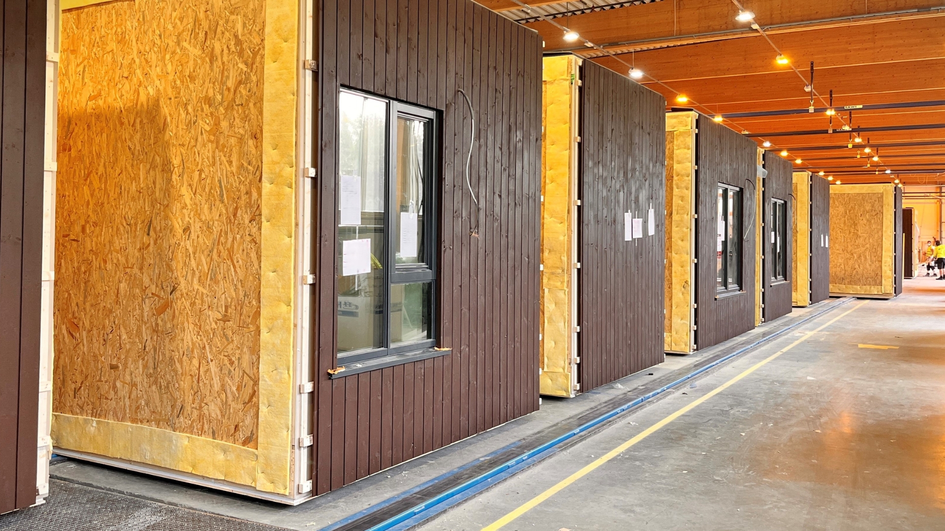 Brown-stained wooden modules are lined up one after another along the factory.