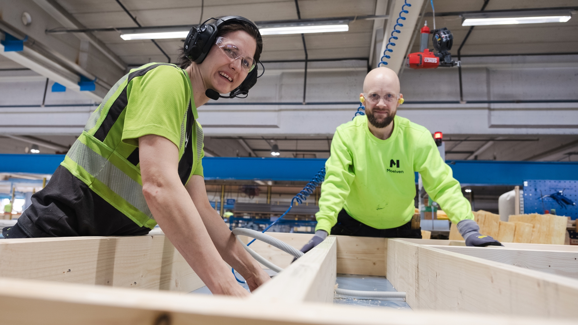 A woman and a man assembling the frame of a building element in a factory.