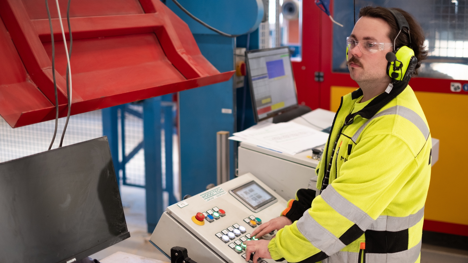 Factory worker wearing hearing protection operating CNC machines.
