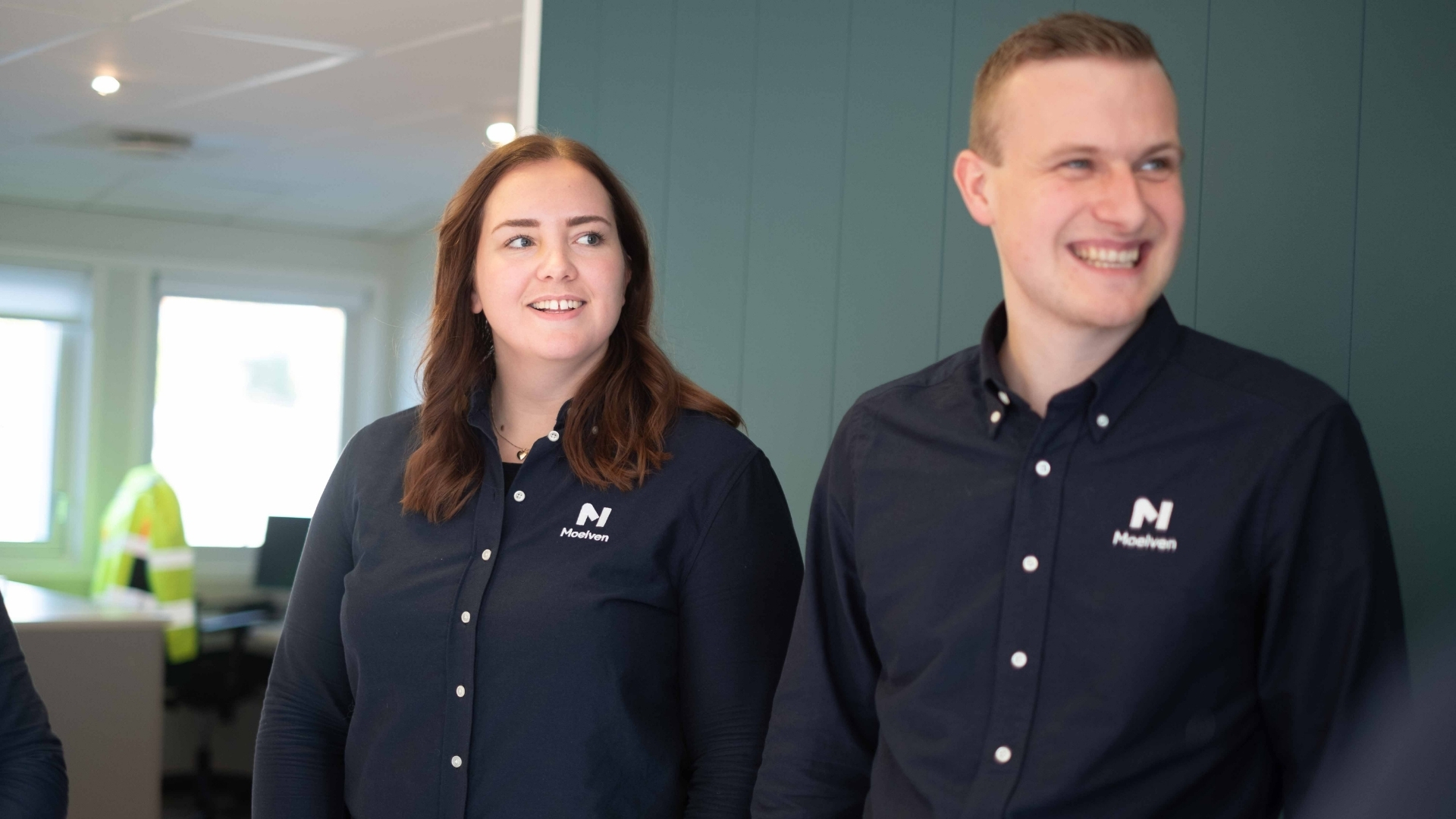 Smiling woman and man in blue Moelven shirts looking to the left.