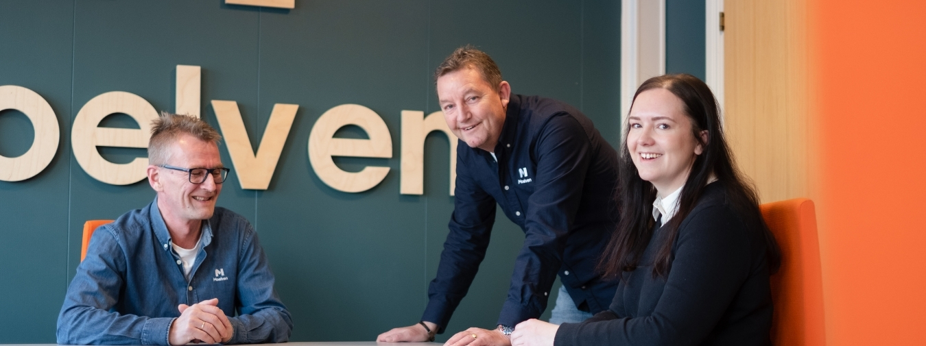 Three smiling colleagues are gathered around a table.