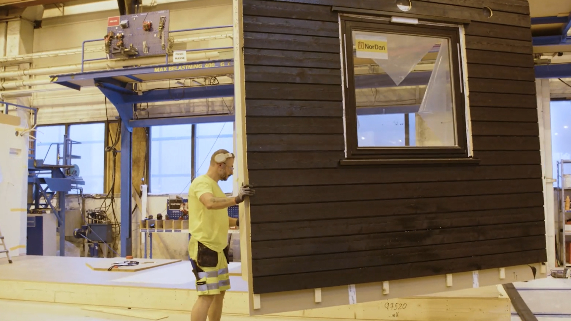 Factory worker holding a wall element suspended by a crane.