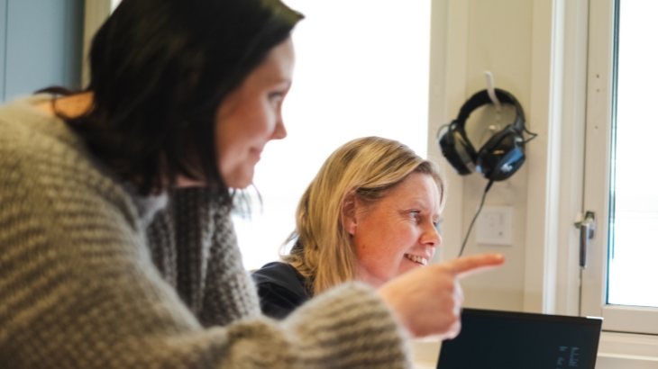 To smilende kolleger som ser mot det samme. Den ene peker.