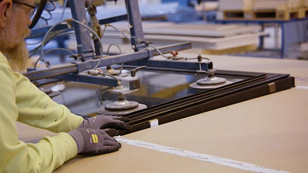 Fabrikkarbeider og robot som plasserer vindu i veggelement.